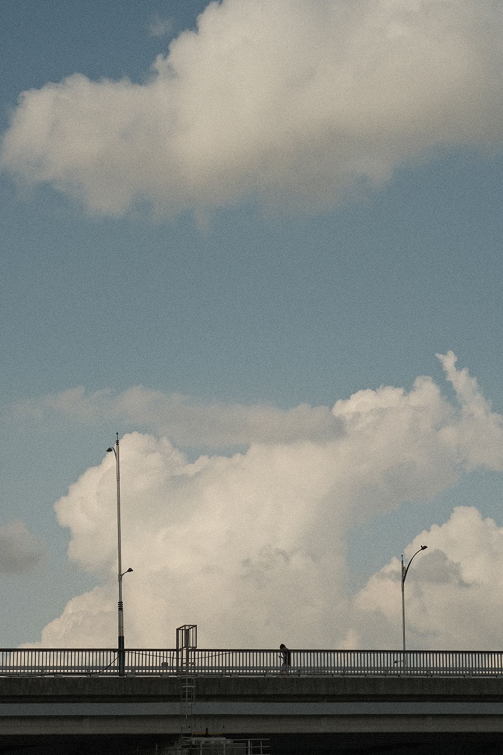 커다란 흰 구름을 배경으로 다리 위를 걸어가는 사람의 모습