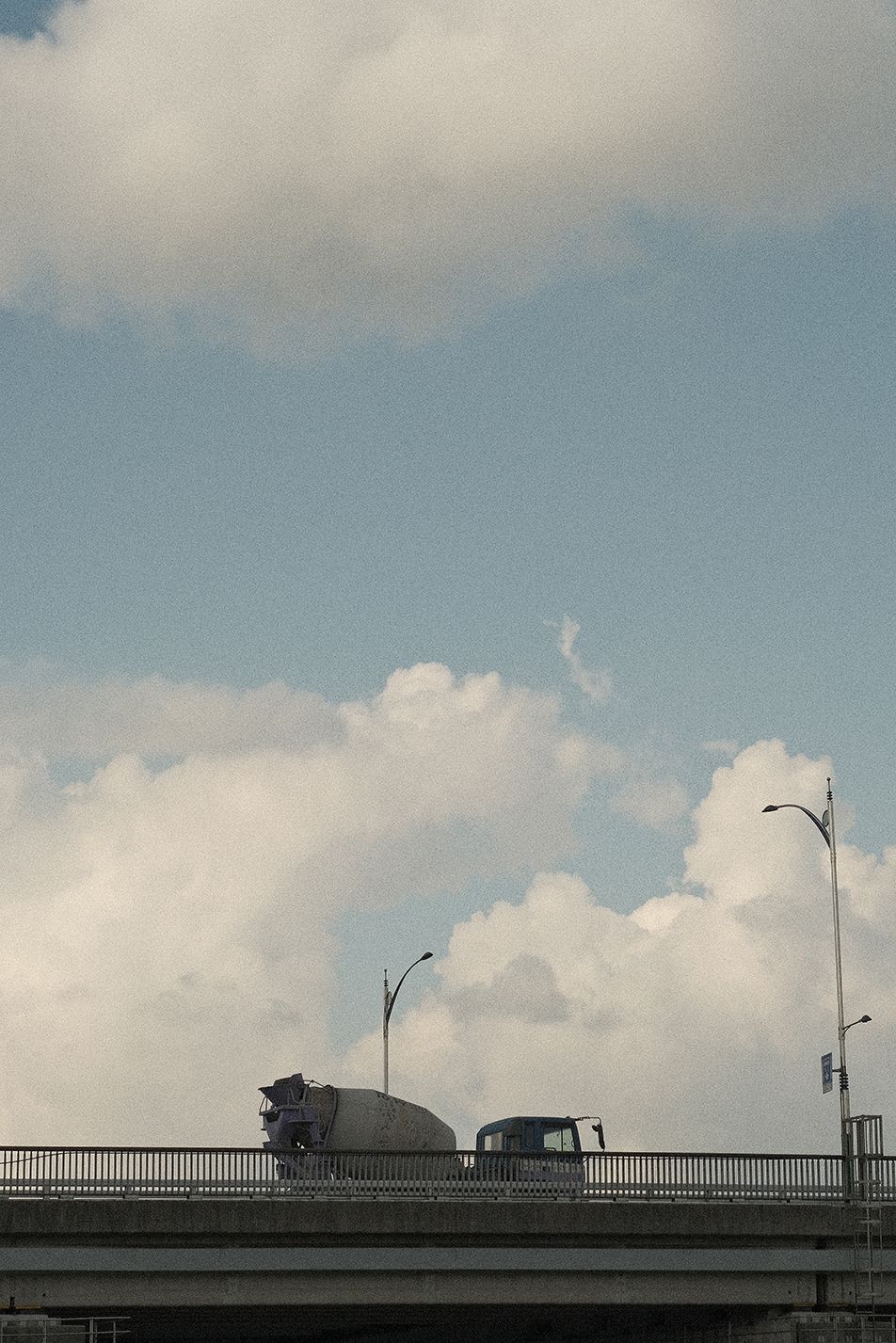 커다란 흰 구름을 배경으로 다리 위를 지나가는 차량의 모습