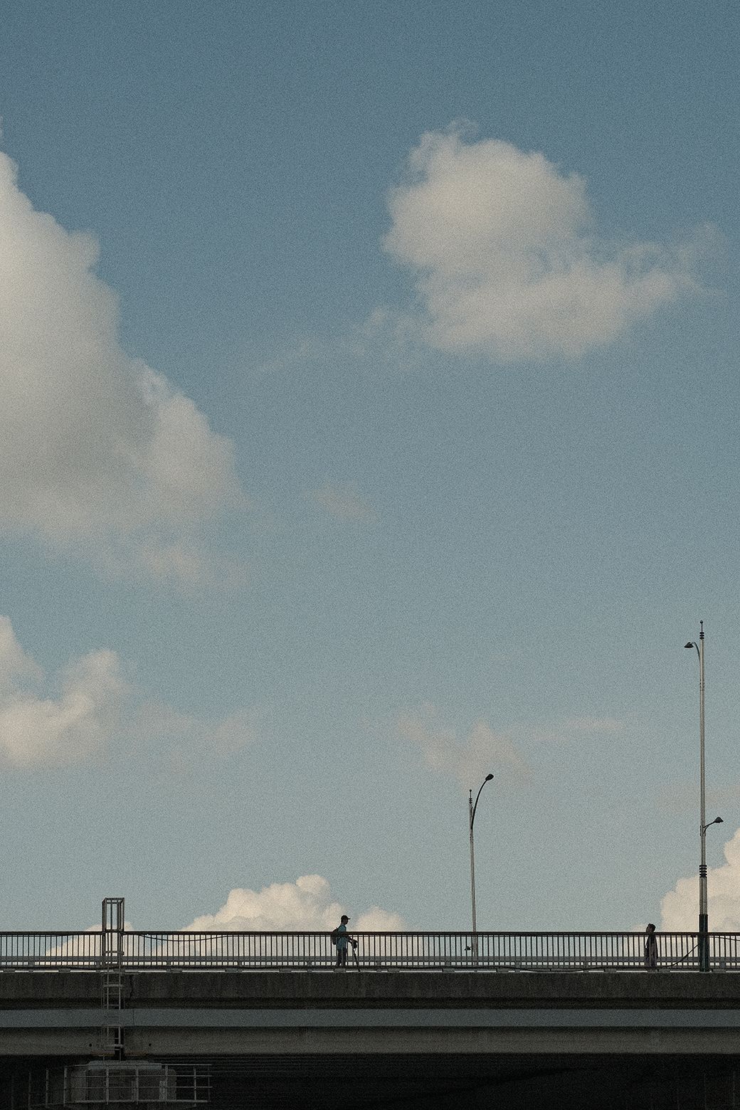 커다란 흰 구름을 배경으로 다리 위를 전동 킥보드를 타고 지나가는 사람의 모습